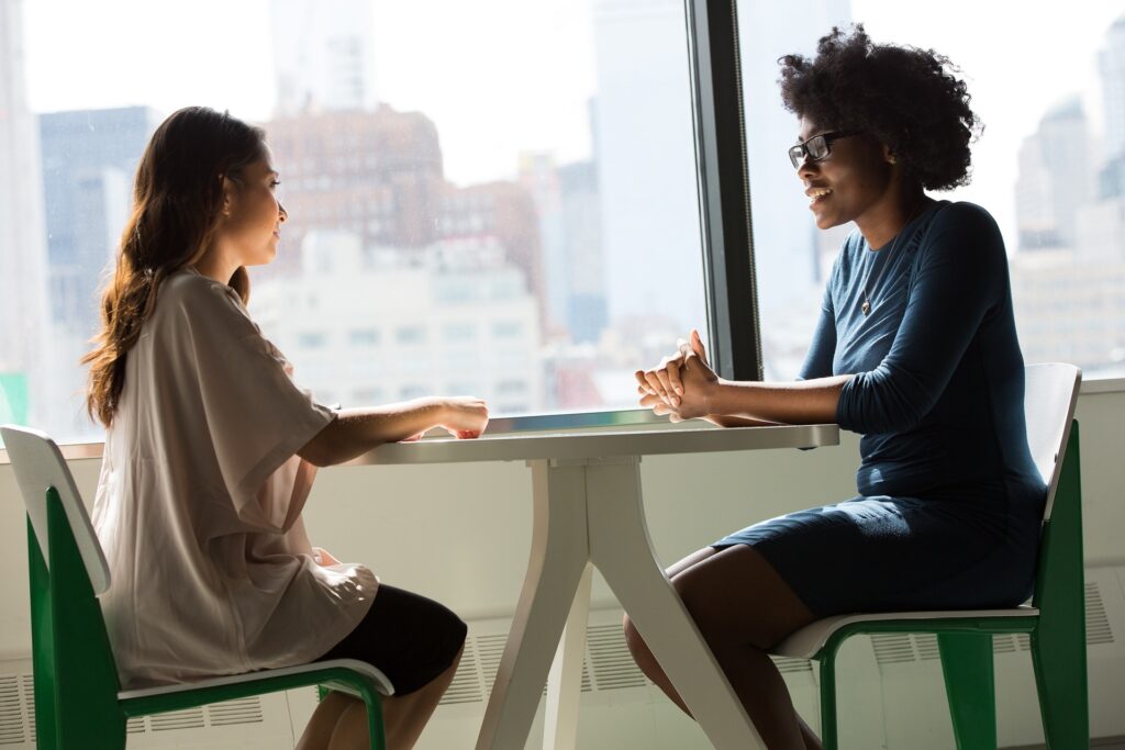 Pour illustrer l'échange verbal avec votre sophrologue, deux femmes sont assises face à face sur des chaises et accoudées à une table.