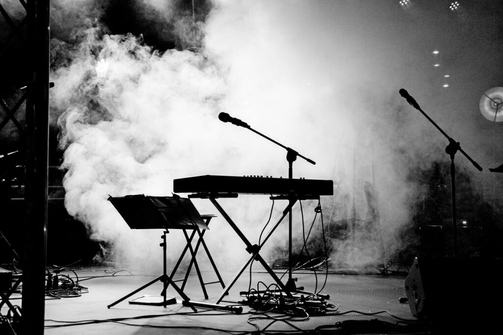 photo en noir et gris d'une scène envahi par la fumée. se détachent en noir sur la fumée blanche un clavier, un tabouret et un micro