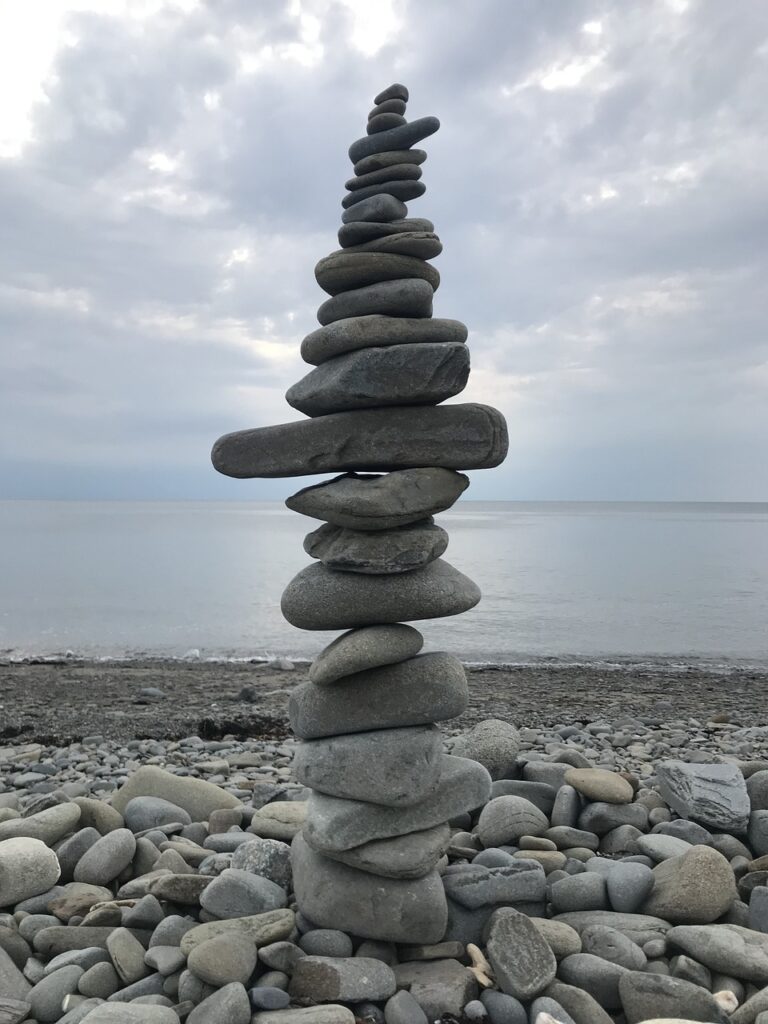 Photo d'un cairn sur une plage de galet pour illustrer comment la sophrologie peut permettre un retour à l'équilibre lorsque l'on souffre de douleurs psychosomatiques.