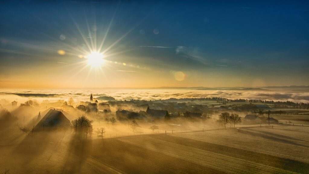 Photo d'un levé de soleil qui chasse la brume sur un village de montagne pour illustrer comment la sophrologie peut réellement améliorer la vie des personnes souffrant de douleur psychosomatique ou psychogènes.